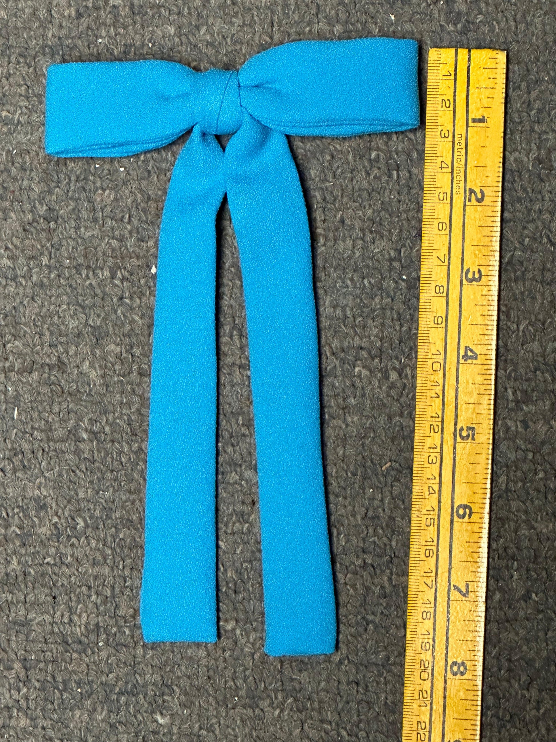 A bow tie from Square Up Fashions' Colonel Ties collection, reminiscent of southern charm, sits next to a yellow measuring tape displaying inches on a gray surface.