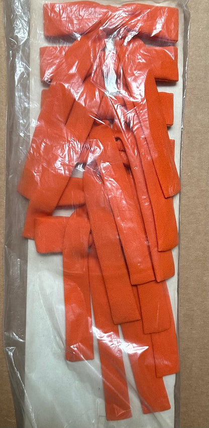 A package of Colonel Ties orange foam corner protectors, from Square Up Fashions, reminiscent of a southern bow tie, is nestled inside a clear plastic bag atop a cardboard surface.