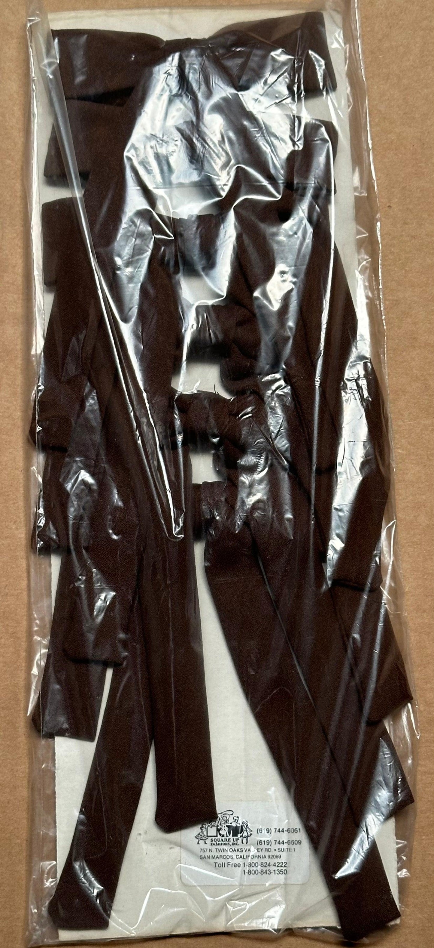 A clear plastic packaging reveals a bag of Colonel Ties made of dark brown leather strips, evoking a classic western look, set against a beige background by Square Up Fashions.