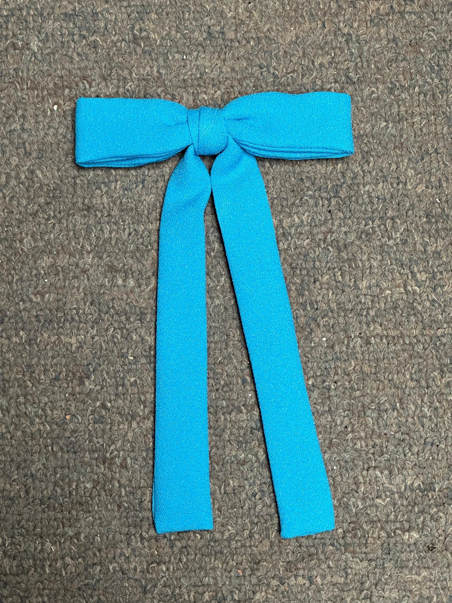 A blue fabric bow from Square Up Fashions' Colonel Ties collection, with long tails reminiscent of a southern bow tie, lies elegantly on a textured gray surface.