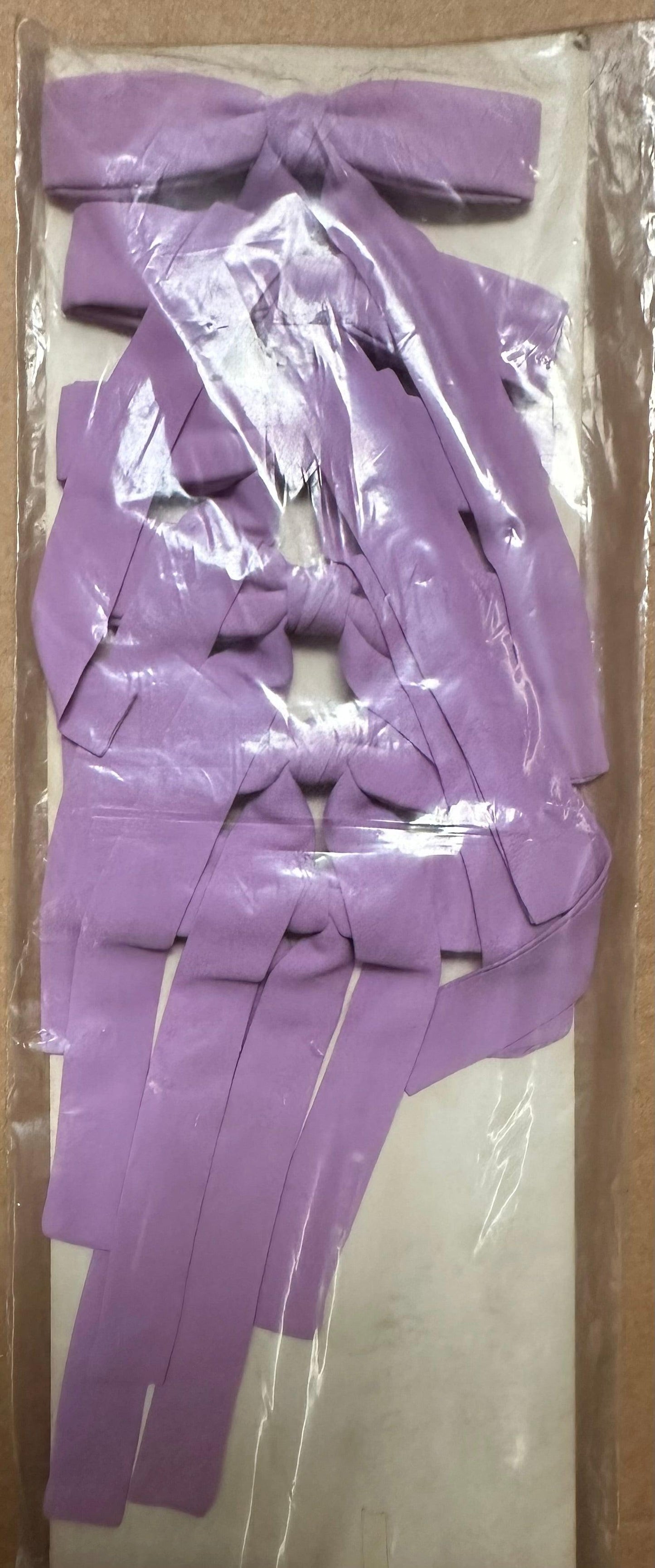 A collection of Colonel Ties ribbons by Square Up Fashions, featuring a western-inspired design in purple, is neatly organized in a pattern and showcased in a plastic package.