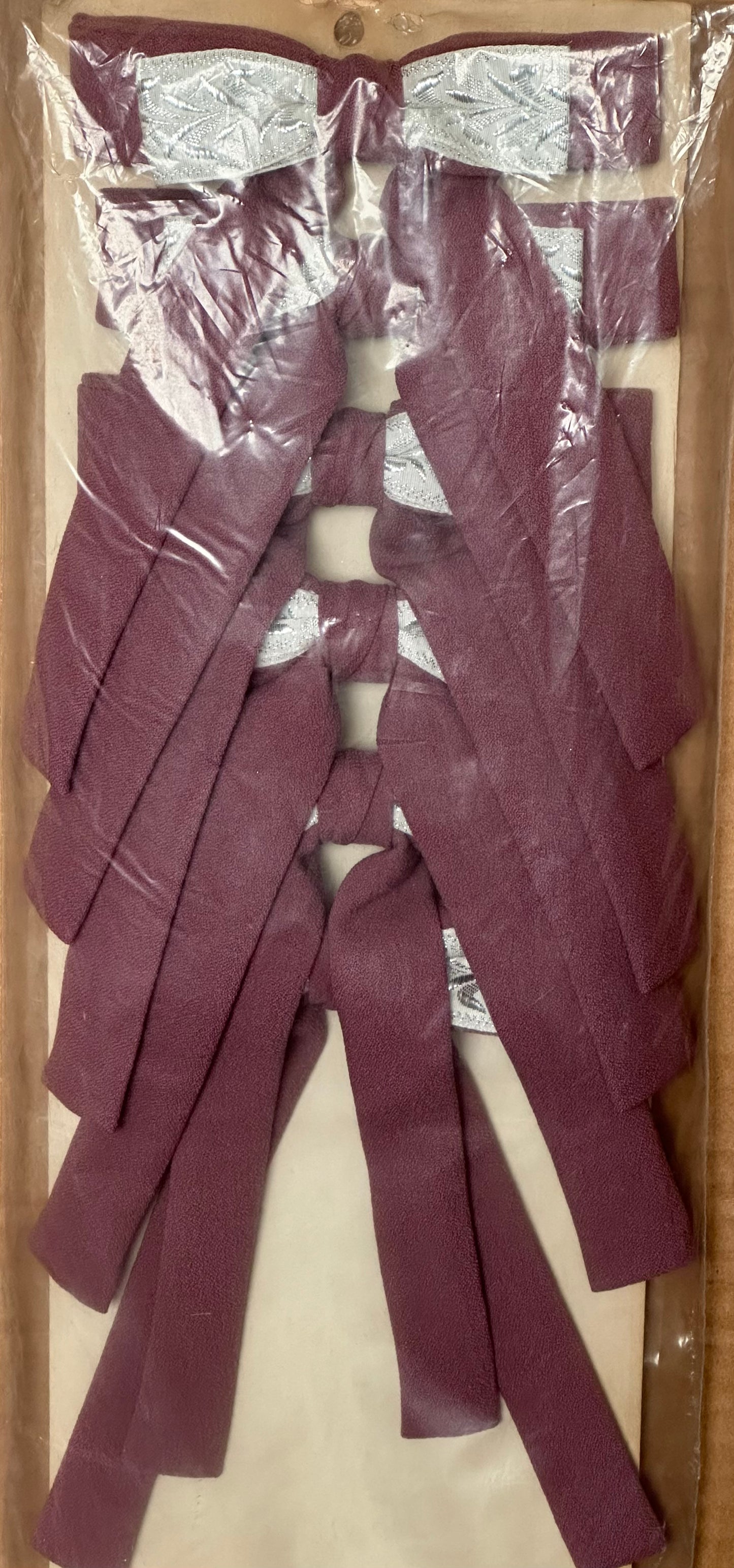 A maroon textile piece from Square Up Fashions, wrapped in plastic, showcases multiple Colonel Ties with southern bow tie designs for a distinct western look.