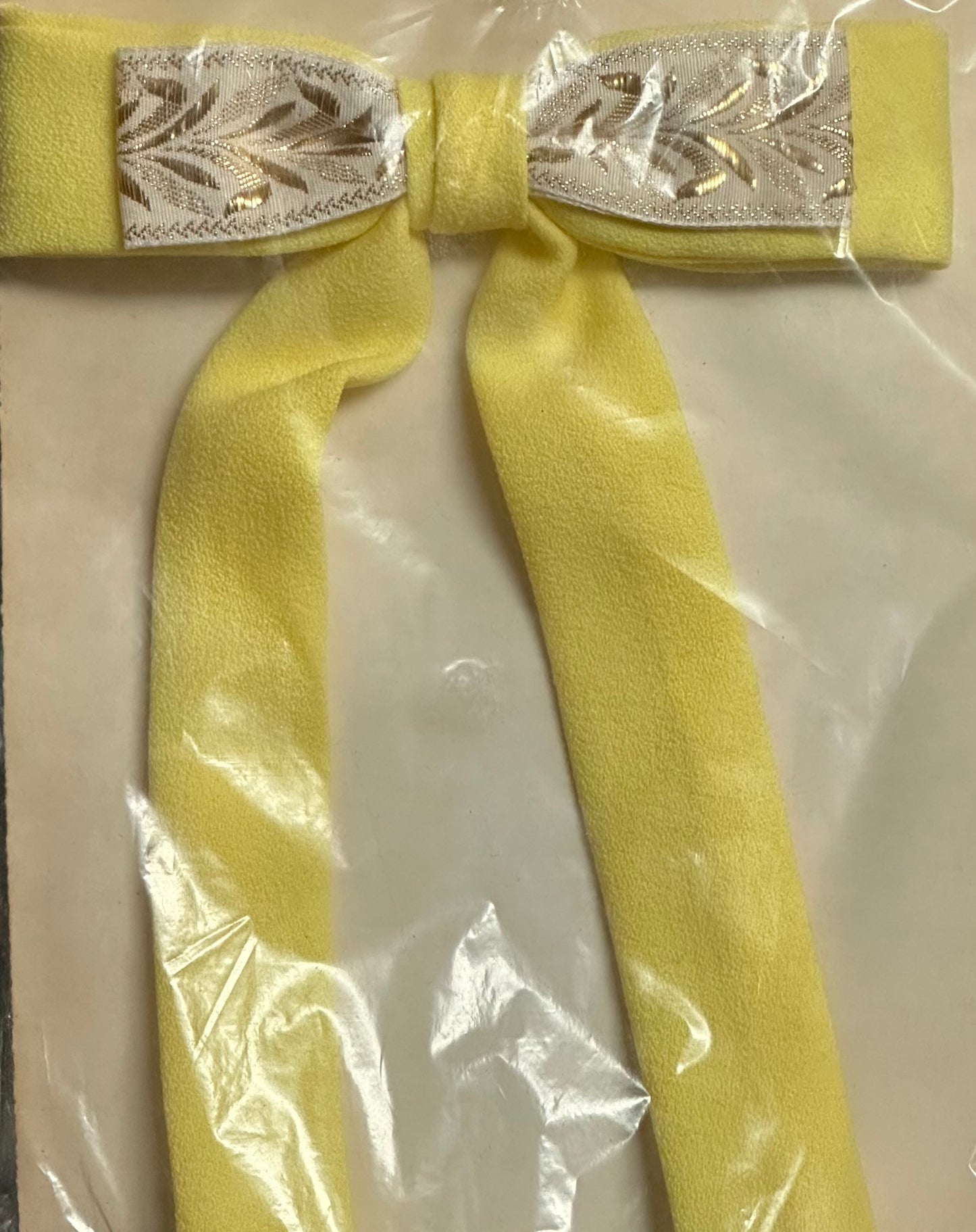 A Colonel Ties bow from Square Up Fashions, featuring a yellow design with a silver-patterned center reminiscent of a southern bow tie, is displayed on a transparent surface.