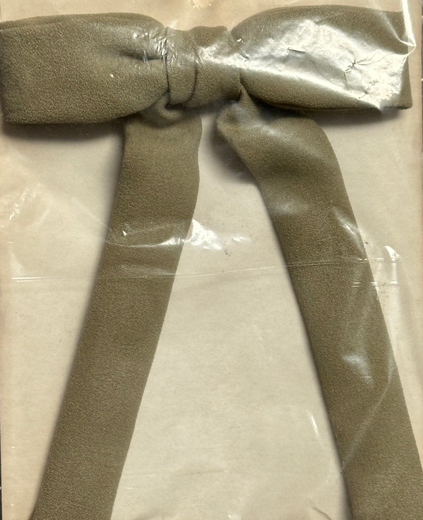 A sealed Colonel Tie by Square Up Fashions, featuring a taupe-colored bow with long tails, evokes a western look on a beige background.