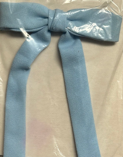 A Colonel Tie by Square Up Fashions in a light blue fabric, styled in a simple southern bow tie design, elegantly displayed on a clear plastic sheet.