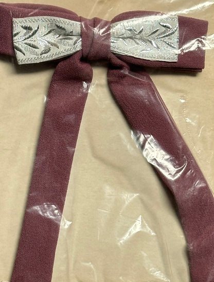 A Colonel Ties bow from Square Up Fashions, featuring a maroon fabric with silver embroidered details reminiscent of a southern bow tie, rests on a beige surface, partially wrapped in clear plastic.