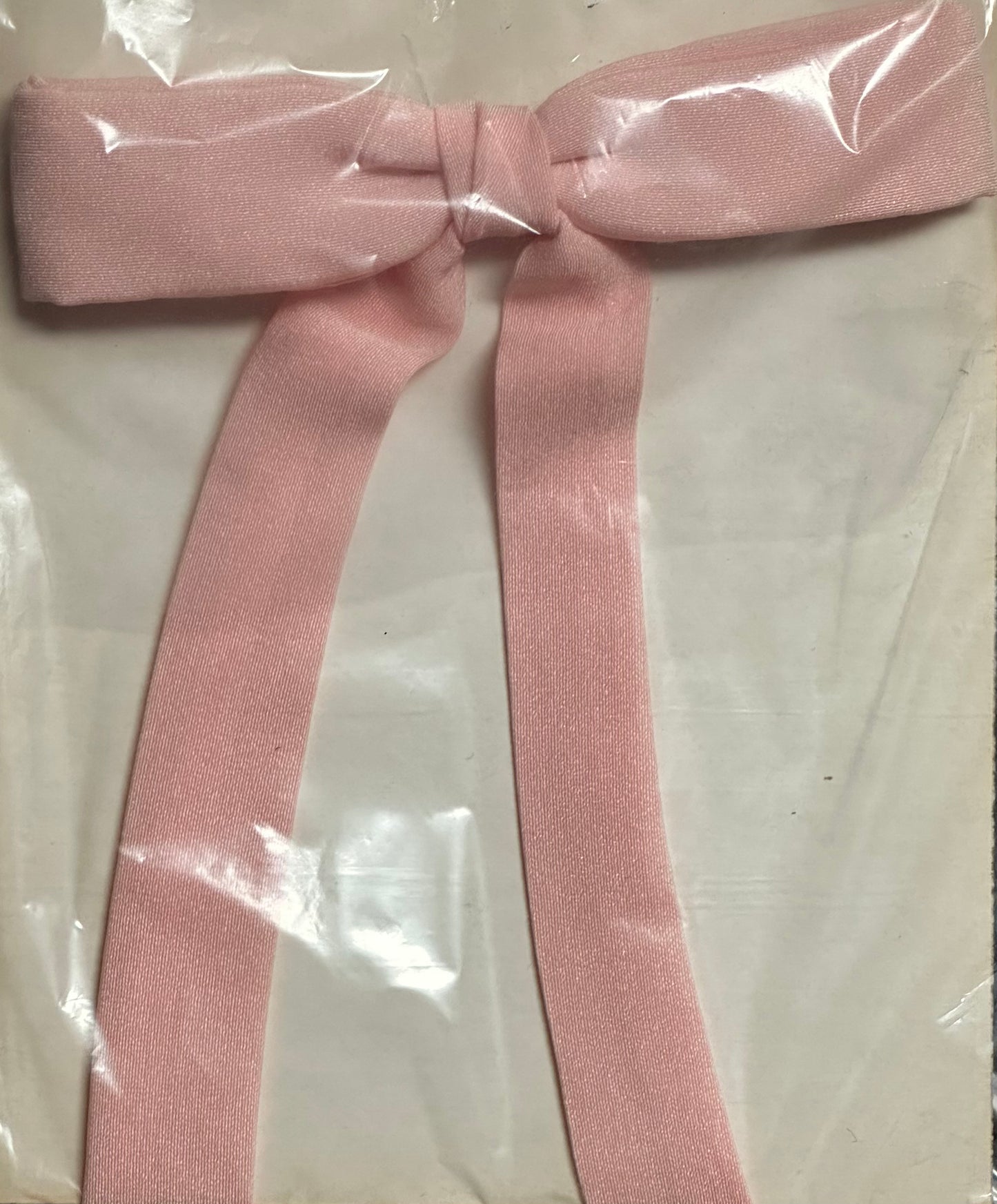 The Colonel Ties from Square Up Fashions, featuring a pink bow with long tails reminiscent of a southern bow tie, rests elegantly on a white surface and is covered in transparent wrapping.