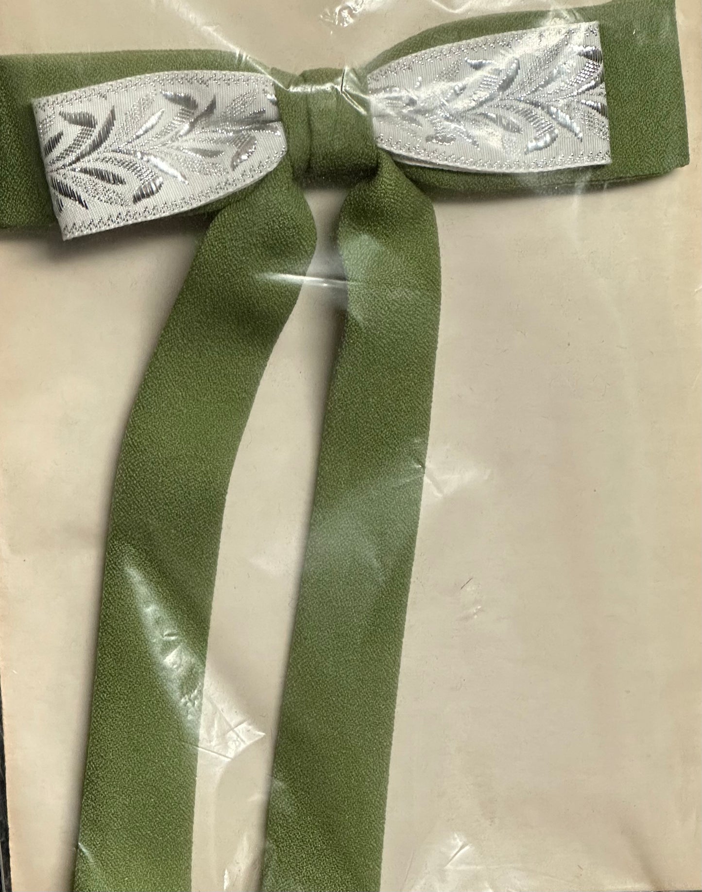 Displayed on a beige background, the Colonel Ties by Square Up Fashions features a green bow with long tails and a white ribbon at the center, capturing the charm of a southern bow tie.