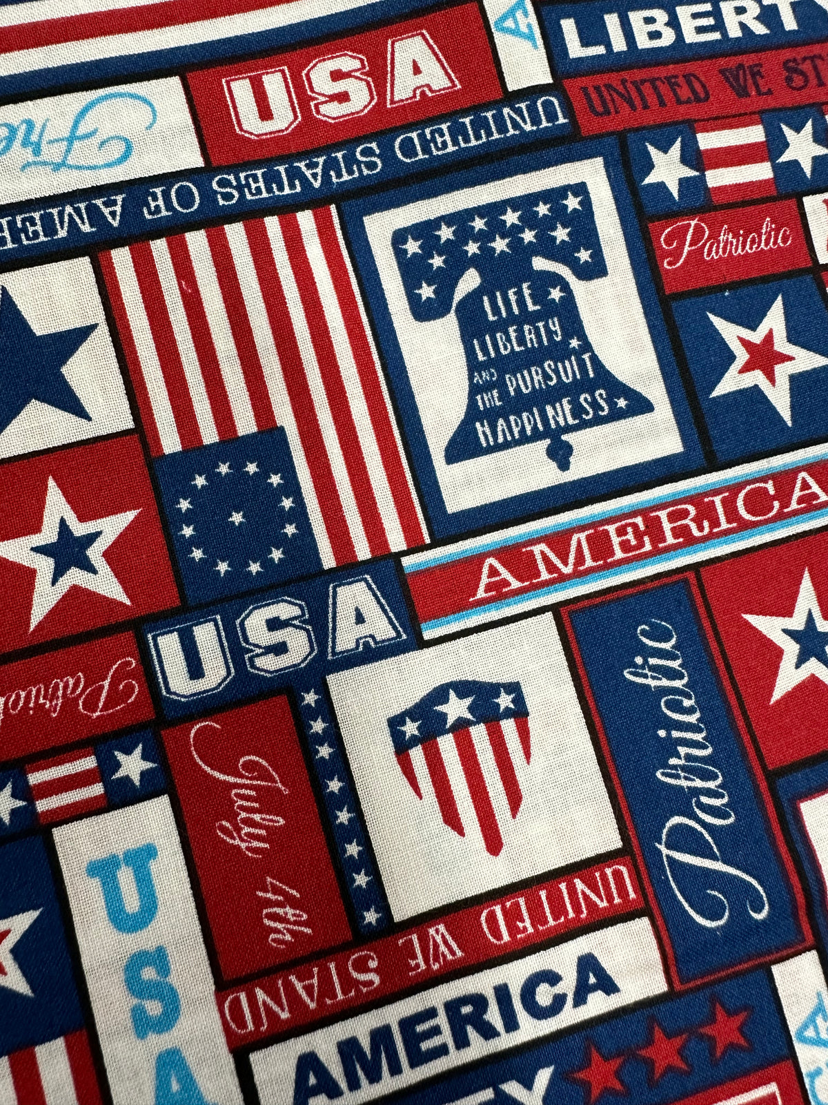 A fabric pattern celebrating American independence with blocks of patriotic symbols and phrases such as &quot;USA,&quot; &quot;America,&quot; &quot;Liberty,&quot; and &quot;Life, Liberty, and the Pursuit of Happiness,&quot; adorned with stars and stripes in red, white, and blue. Ideal for a 12-gore skirt showcasing true patriotism like the July 4th Square Dance Skirt by Square Up Fashions.